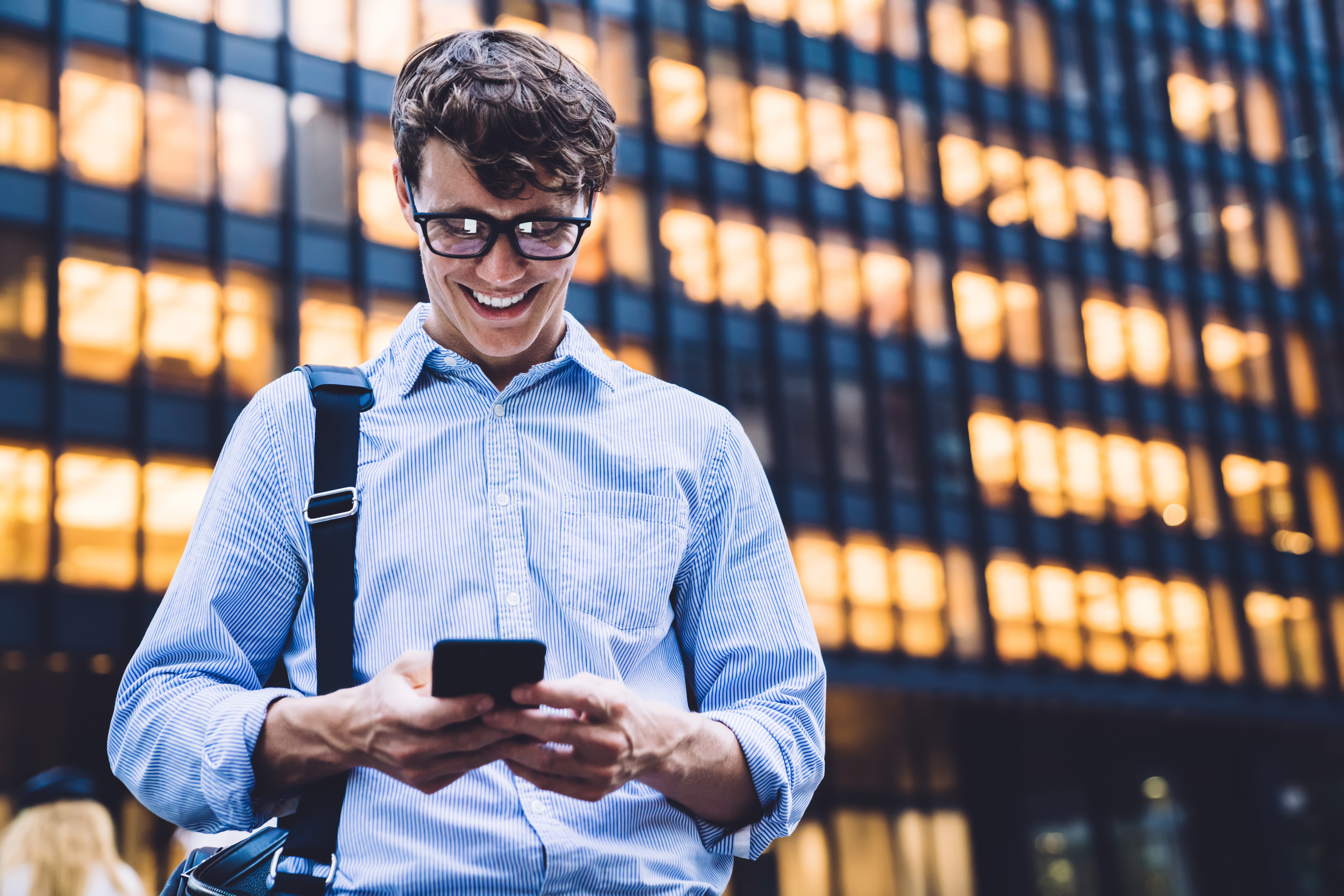 young man in glasses smiling looking at his phone